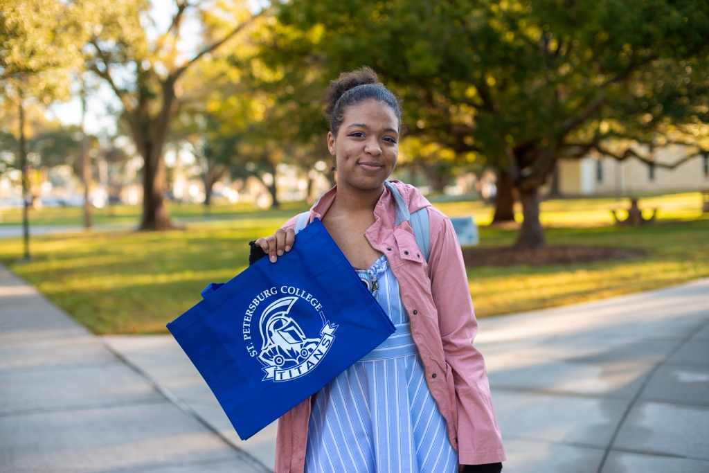 A black, female student standing outside smiling while holding a blue SPC Titans bag.